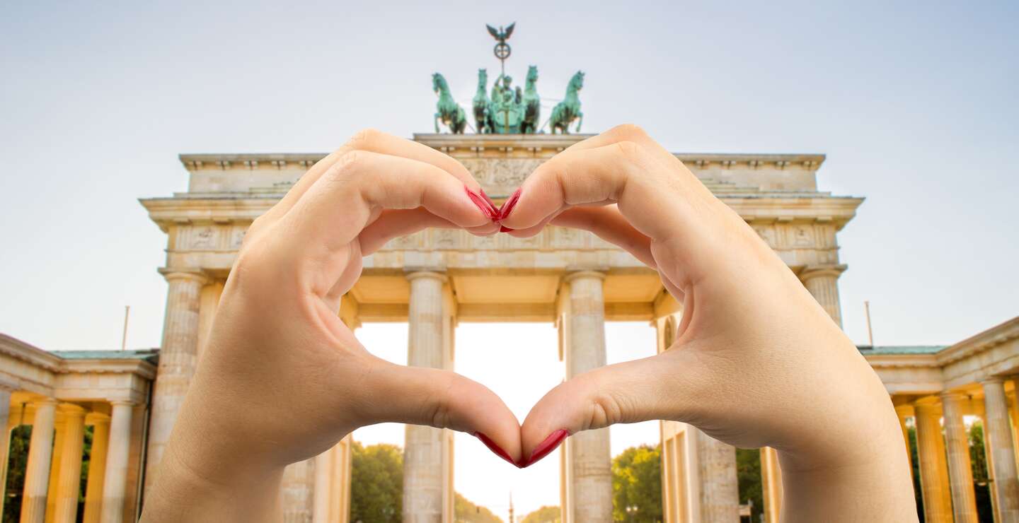 Hande mit rot lackierten Fingernägeln formen ein Herz vor dem Brandenburger Tor in Berlin  | © Gettyimages.com/Manuel-F-O