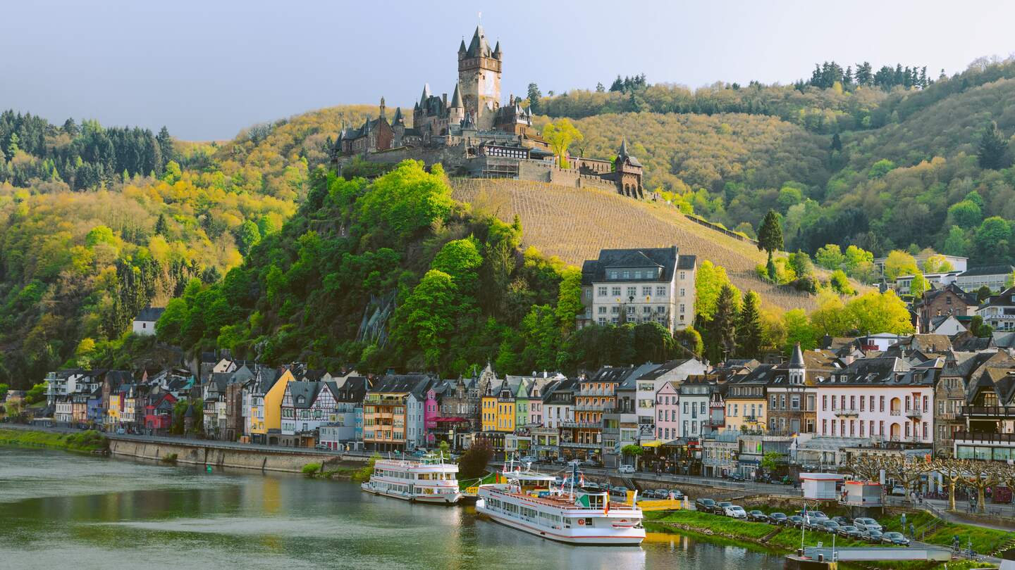 Wunderschoener Stadtblick auf die historische Altstadt von Cochem mit den typischen fachwerkbunten Haeusern, Hotels und Restaurants, Wahrzeichen der Reichsburg auf einem Berg, Mosel im sonnigen Fruehling  | © GettyImages.com/serts