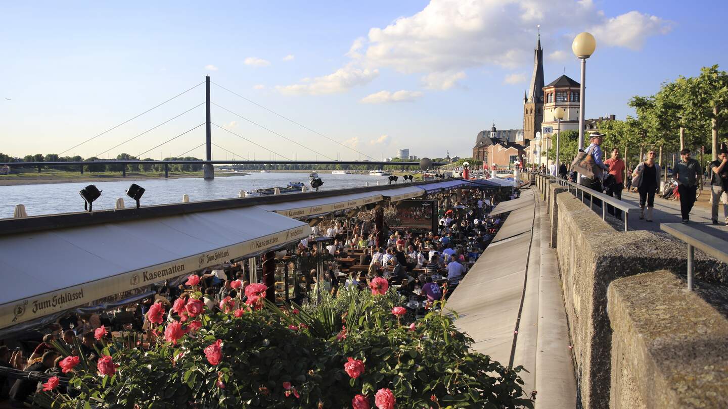 Bars und Restaurants entlang des Rheins in Duesseldorf und Menschen, die auf der Promenade darueber spazieren gehen | © Gettyimages.com/Lux_D