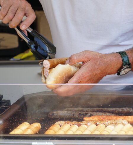 Ein Mann bereitet und eine Grillwurst in einem Brotbroetchen zu. Die "Lange Rote" ist typisch fuer Freiburg | © Gettyimages.com/Lucia Gajdosikova