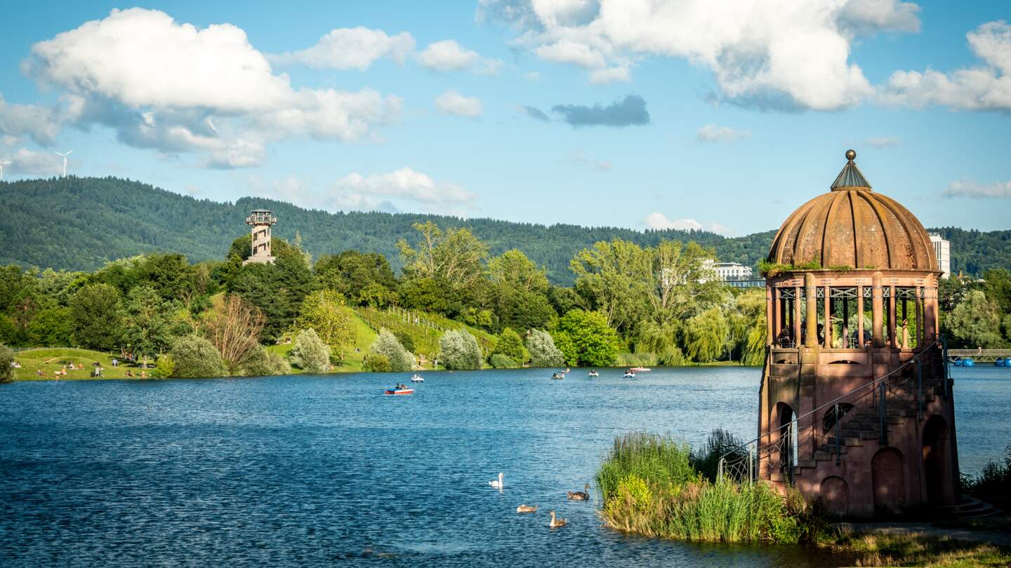 Buntes Panorama des Flueckiger Sees mit zwei Aussichtstuermen am Seepark in Freiburg | © GettyImages.com/Andreas Naegeli