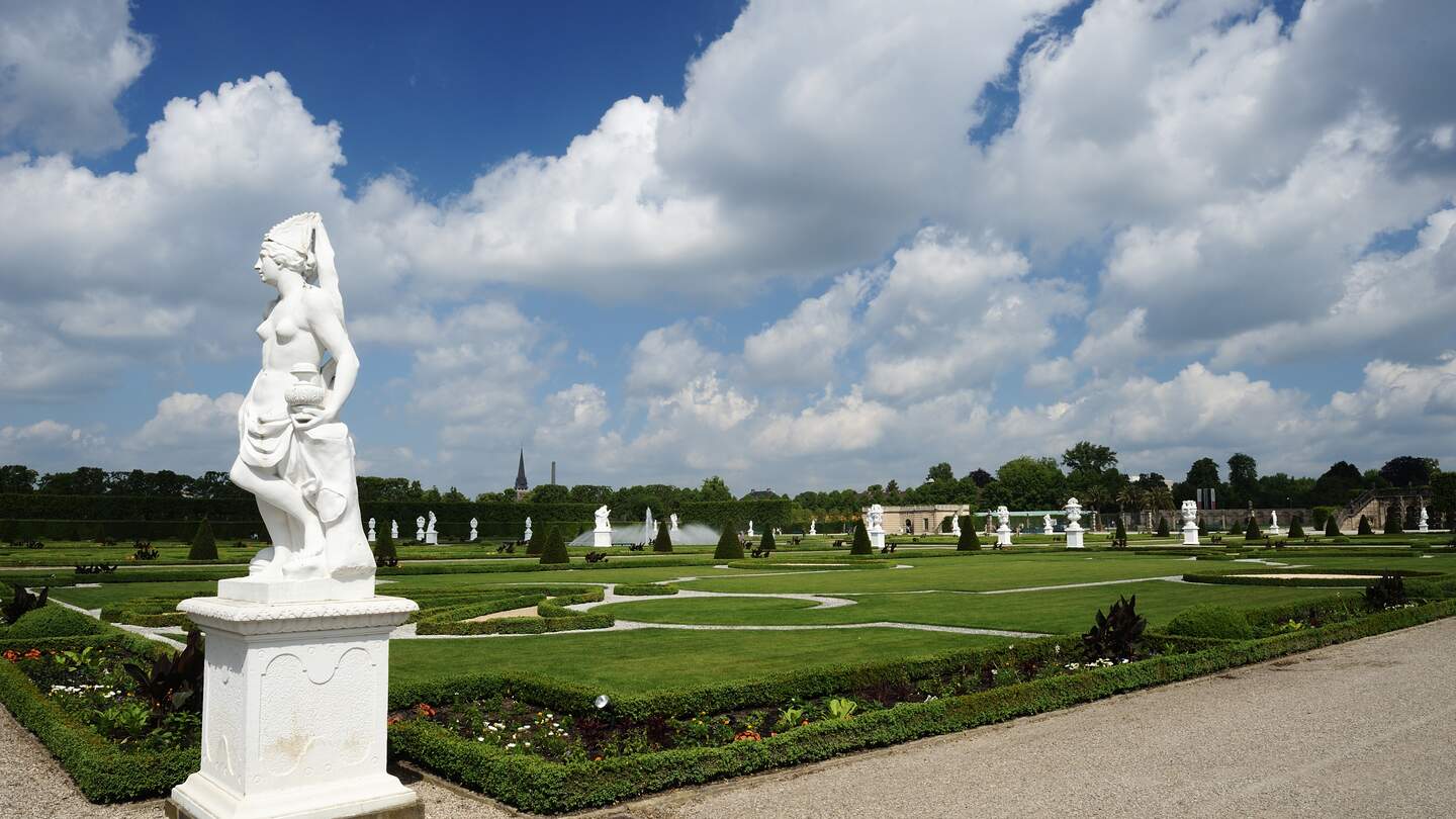 Blick auf die Koeniglichen Gaerten von Herrenhausen in Hannover mit bewoelktem Himmel mit einer Statue im Vordergrund | © Gettyimages.com/technotr
