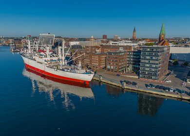 Luftaufnahme des groessten Museumsfrachtschiffs der Welt, das im Kieler Hafen vor Anker liegt. Ein weisses und rotes Schiff im Hafen von Kiel. | © Gettyimages.com/frederick doerschem
