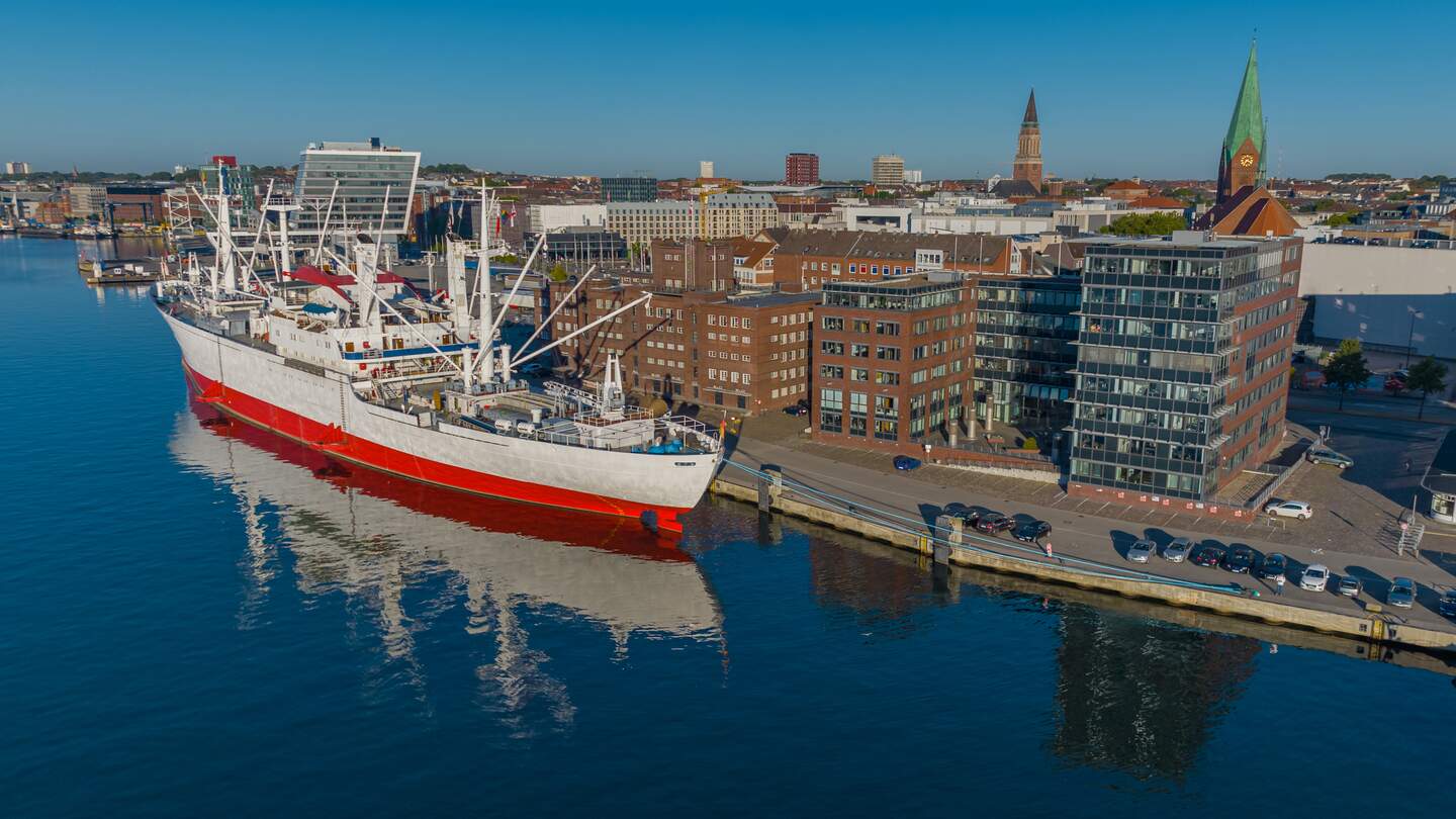 Luftaufnahme des groessten Museumsfrachtschiffs der Welt, das im Kieler Hafen vor Anker liegt. Ein weisses und rotes Schiff im Hafen von Kiel. | © Gettyimages.com/frederick doerschem