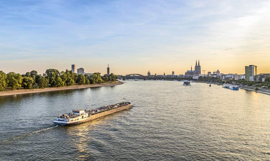 Luftaufnahme über dem Rhein mit Blick auf ein Schiffund die Skyline von Köln bei Sonnenuntergang | © Gettyimages.com/Meinzahn