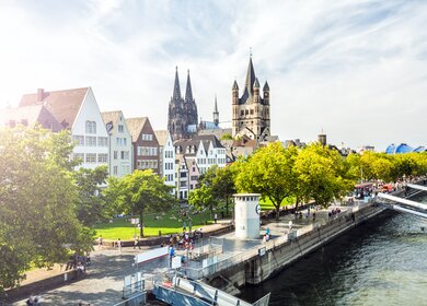 Menschen laufen auf der Rheinpromenade in Köln, der Blick auf die Kölner Altstadt | © Gettyimages.com/querbeet
