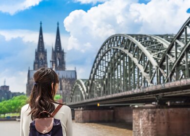 Eine Frau von hinten die auf den Koelner Dom und Hohenzollenbrueke ueber den Rhein in Koeln blickt | © gettyimages.com/75tiks