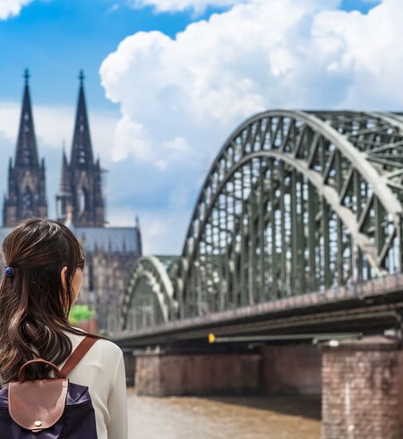 Eine Frau von hinten die auf den Koelner Dom und Hohenzollenbrueke ueber den Rhein in Koeln blickt | © gettyimages.com/75tiks