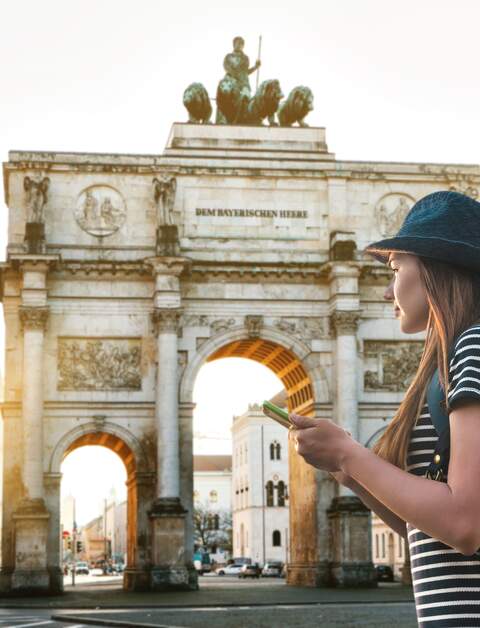 Eine Frau mit einem Rucksack betrachtet den Trimphbogen in München  | © Gettyimages.com/franz12