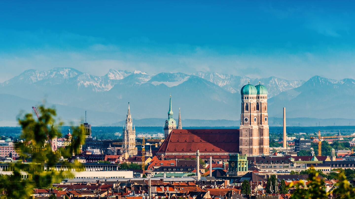Die Skyline von München mit der Frauenkriche bei schönem Wetter mit Bergen im Hintergrund | © Gettyimages.com/jotily