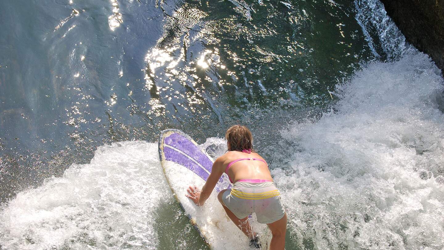Aufsicht auf eine Surferin im Isarkanal in München mit Bikini und Shorts an einem Sommertag | © Gettyimages.com/raku52