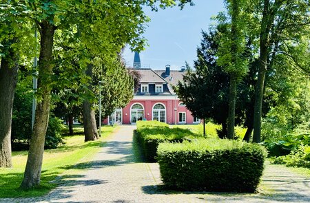 Die LUDWIGGALERIE im roten Oberhausener Schloss, welches eingebettet ist in einen Park mit grünen Bäumen | © Michelle Khan