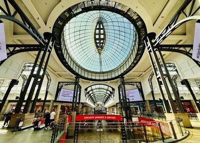 Ein großes Einkaufszentrum mit einer weitläufigen Glaskuppel, das moderne Architektur und lebendige Einkaufsbereiche präsentiert. | © Michelle Khan