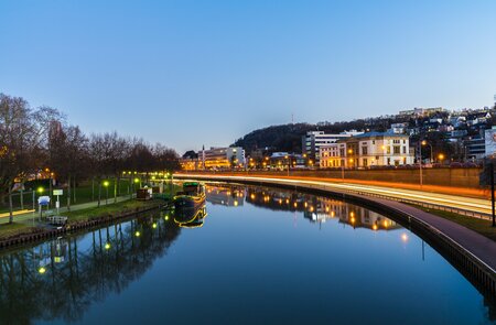 Naechtlicher Verkehr und Gebaeude, die sich im Flusswasser der Saar in Saarbruecken in magischer Atmosphaere spiegeln | © Gettyimages.com/Simon Dux