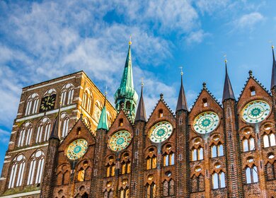 Fassade des historischen Rathauses in Stralsund im Stil der norddeutschen Backsteingotik mit der Nikolaikirche im Hintergrund | © Gettyimages.com/A-Tom