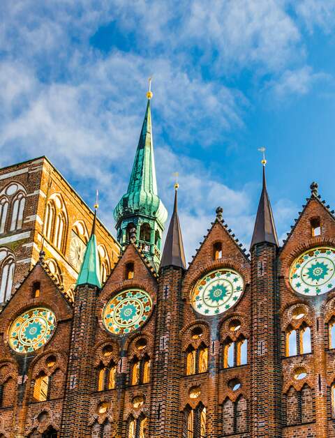 Fassade des historischen Rathauses in Stralsund im Stil der norddeutschen Backsteingotik mit der Nikolaikirche im Hintergrund | © Gettyimages.com/A-Tom