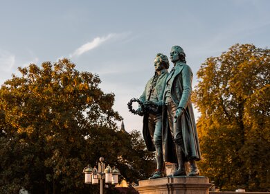 Goethe-Schiller-Denkmal in Weimar im Sonnenlicht am Morgen unter blauem Himmel | © Gettyimages.com/Robert Ruidl