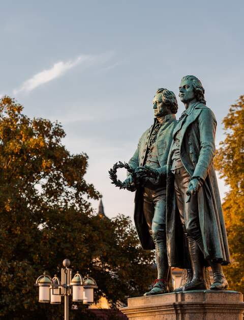 Goethe-Schiller-Denkmal in Weimar im Sonnenlicht am Morgen unter blauem Himmel | © Gettyimages.com/Robert Ruidl