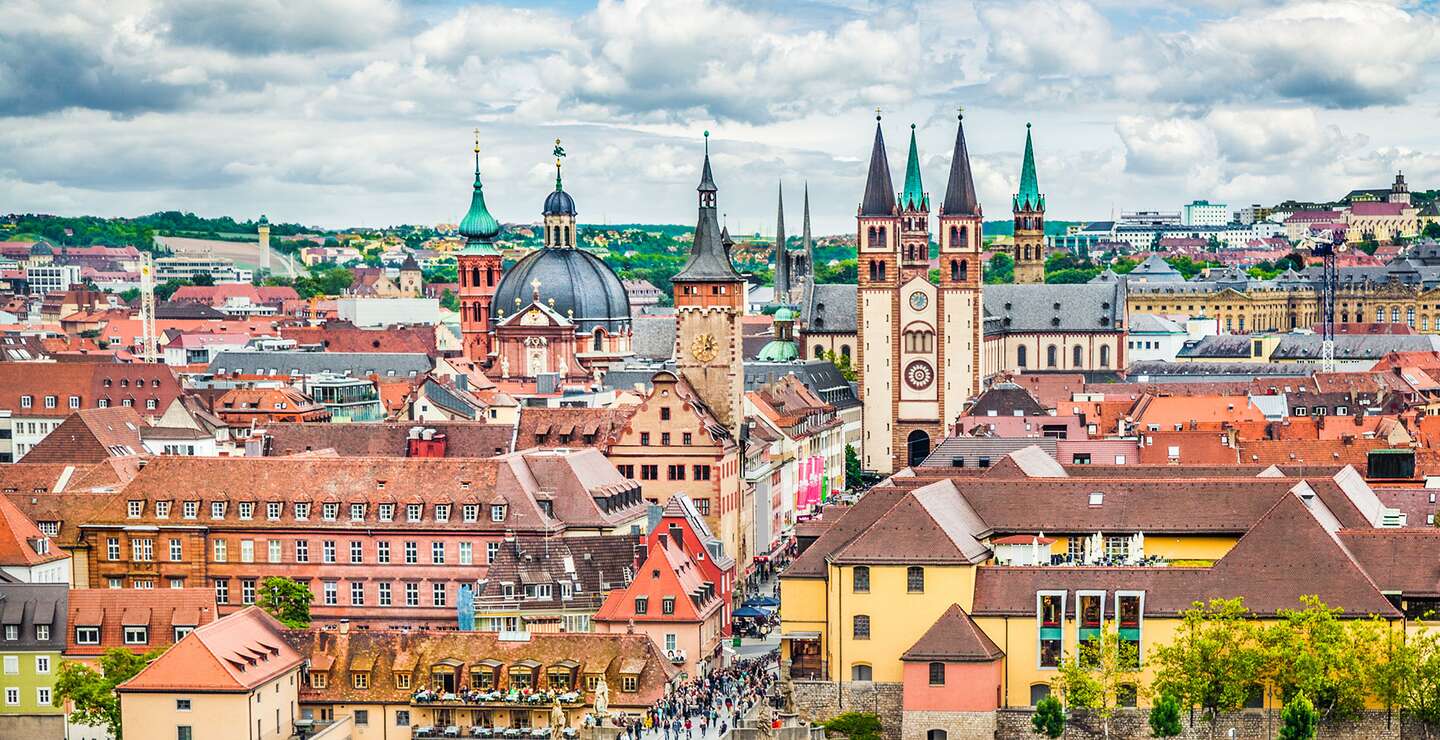  Panoramaansicht der Stadt Wuerzburg in Deutschland, mit einer Bruecke ueber einen Fluss, die zu einem Bereich mit verschiedenen historischen Gebaeuden fuehrt, darunter markante Kirchtuerme und Tuerme. | © Gettyimages.com/JR Photography