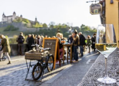Menschen stehen an einem Weinlokal auf der Alten Mainbruecke in Wuerzburg und unterhalten sich | © Gettyimages.com/TomekD76