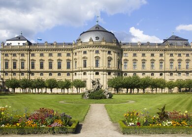 Frontalansicht der Residenz Wuerzburg mit Blick auf den Felsenbrunnen und bluehende Blumen | © Gettyimages.com/Lichtspieler