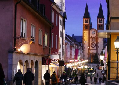 Beleuchtete historische Gebaeude, Tuerme und Kirchen mit reflektierenden Lichtern auf Kopfsteinpflaster in Wuerzburg am Abend | © Gettyimages.com/Hartmut Kosig
