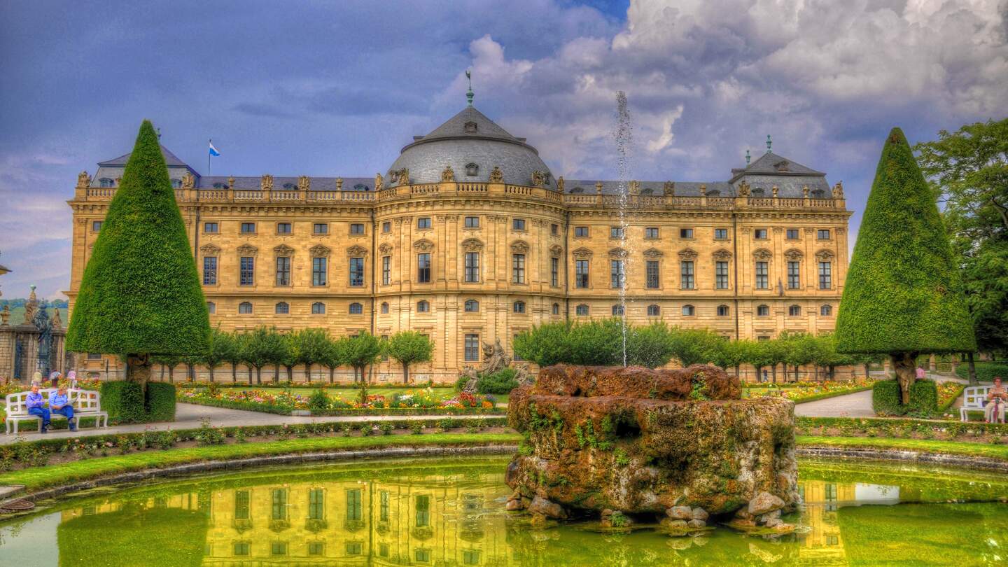 Frontalansicht der Residenz Wuerzburg mit Blick auf den Felsenbrunnen und bluehende Blumen | © Gettyimages.com/Eagle2308