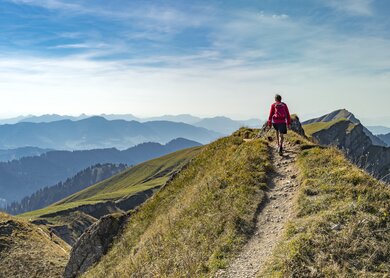 Eine aeltere Frau wandert im Herbst auf dem Grat der Nagelfluhkette bei Oberstaufen im Allgaeu, Bayern, Deutschland, mit dem Hochgrats-Gipfel im Hintergrund. | © Gettyimages.com/Uwe Moser