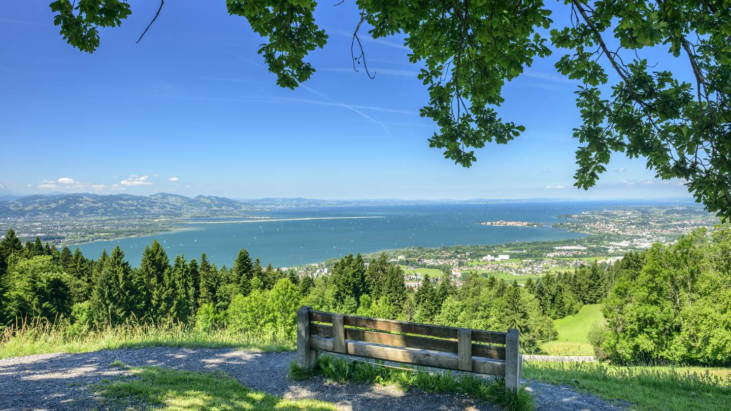 Panoramablick vom idyllischen Bergdorf Eichenberg in Vorarlberg auf den Bodensee. Es gibt eine Bank im Vordergrund und den Bodensee mit der deutschen und der Schweizer Küste im Hintergrund. | © Gettyimages.com/Kemter