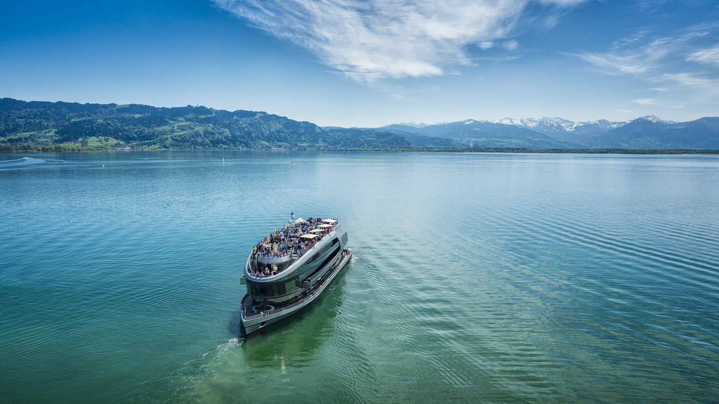 Drohnenaufnahme eines Ausflugsbootes auf dem Bodensee mit vollbesetztem Aussichtsdeck an einem sonnigen Sommertag | © Gettyimages.com/no_limit_pictures