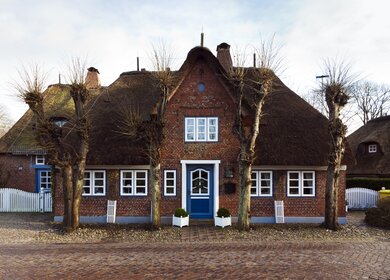 Friesisches Reetdachhaus hinter einer gepflasterten Strasse in Nieblum auf Foehr, Schleswig-Holstein | © Gettyimages.com/eyewave