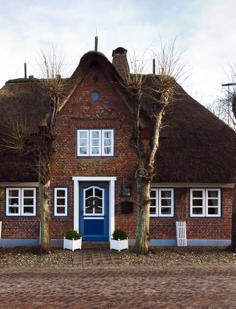 Friesisches Reetdachhaus hinter einer gepflasterten Strasse in Nieblum auf Foehr, Schleswig-Holstein | © Gettyimages.com/eyewave