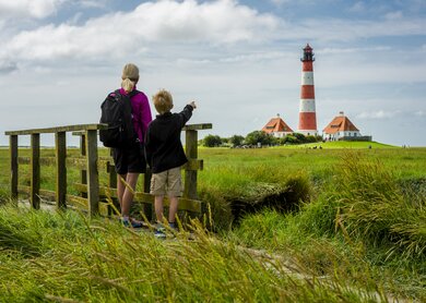 Frau und Junge stehen auf einer kleinen Bruecke und schauen in Richtung des Leuchturms von Westhever | © Gettyimages.com/no_limit_pictures