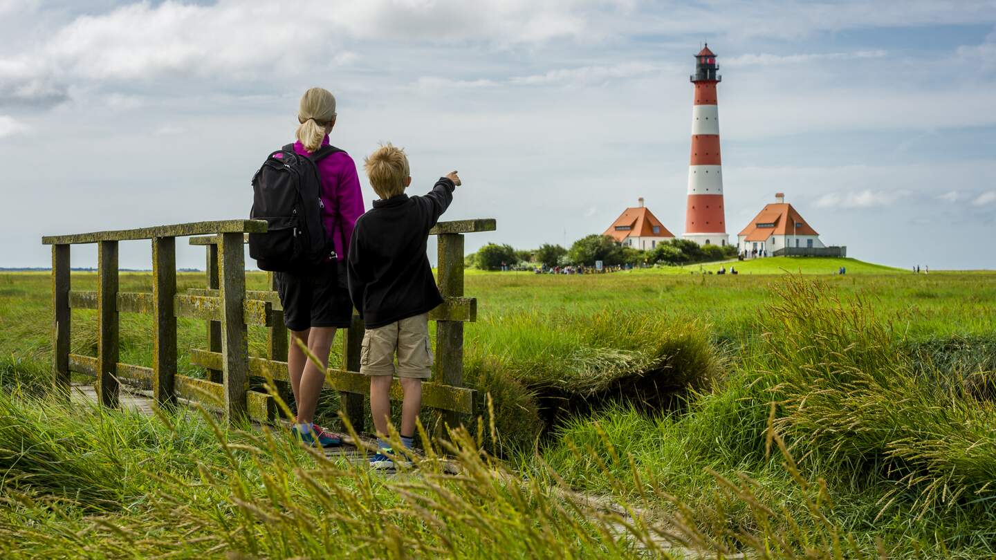 Frau und Junge stehen auf einer kleinen Bruecke und schauen in Richtung des Leuchturms von Westhever | © Gettyimages.com/no_limit_pictures