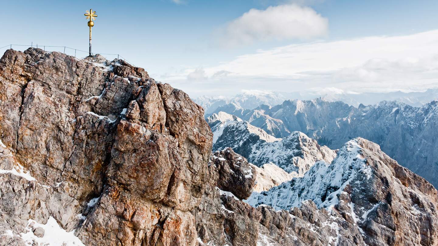 Der hoechste Berg Deutschlands, die Zugspitze, mit goldenem Gipfelkreuz und schneebedeckten Gipfeln bei Sonnenschein | © Gettyimages.com/Alexander Reshnya