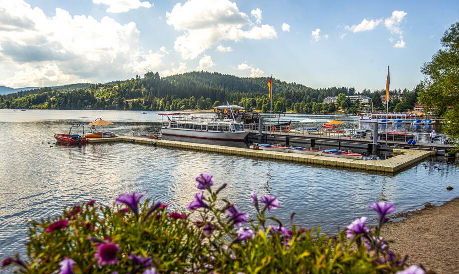 Blick auf einen Bootsanleger mit Booten auf dem Titisee bei Sonnenschein und leichten Wolken | © Gettyimages.com/Wirestock