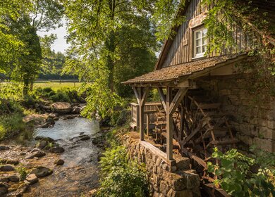 Traditionelle Wassermühle entlang eines Baches, umgeben von Baeumen und Wiesen. Die beruehmte Rainbauernmuehle bei Ottenhoefen, Baden-Wuerttemberg, Deutschland | © Gettyimages.com/connypokorny