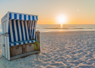 Blau-weiss gestreifter Strandkorb bei Sonnenuntergang auf Sylt | © Gettyimages.com/undefined undefined