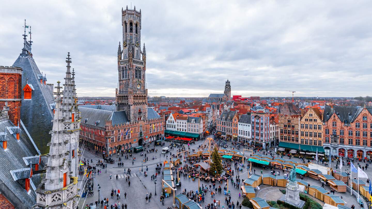 In Bruegge stehen Buden und ein Weihnachtsbaum auf dem grossen Markt. Viele Besucher sind auf dem Weihnachtsmarkt.  | © Gettyimages.com/SilvanBachmann