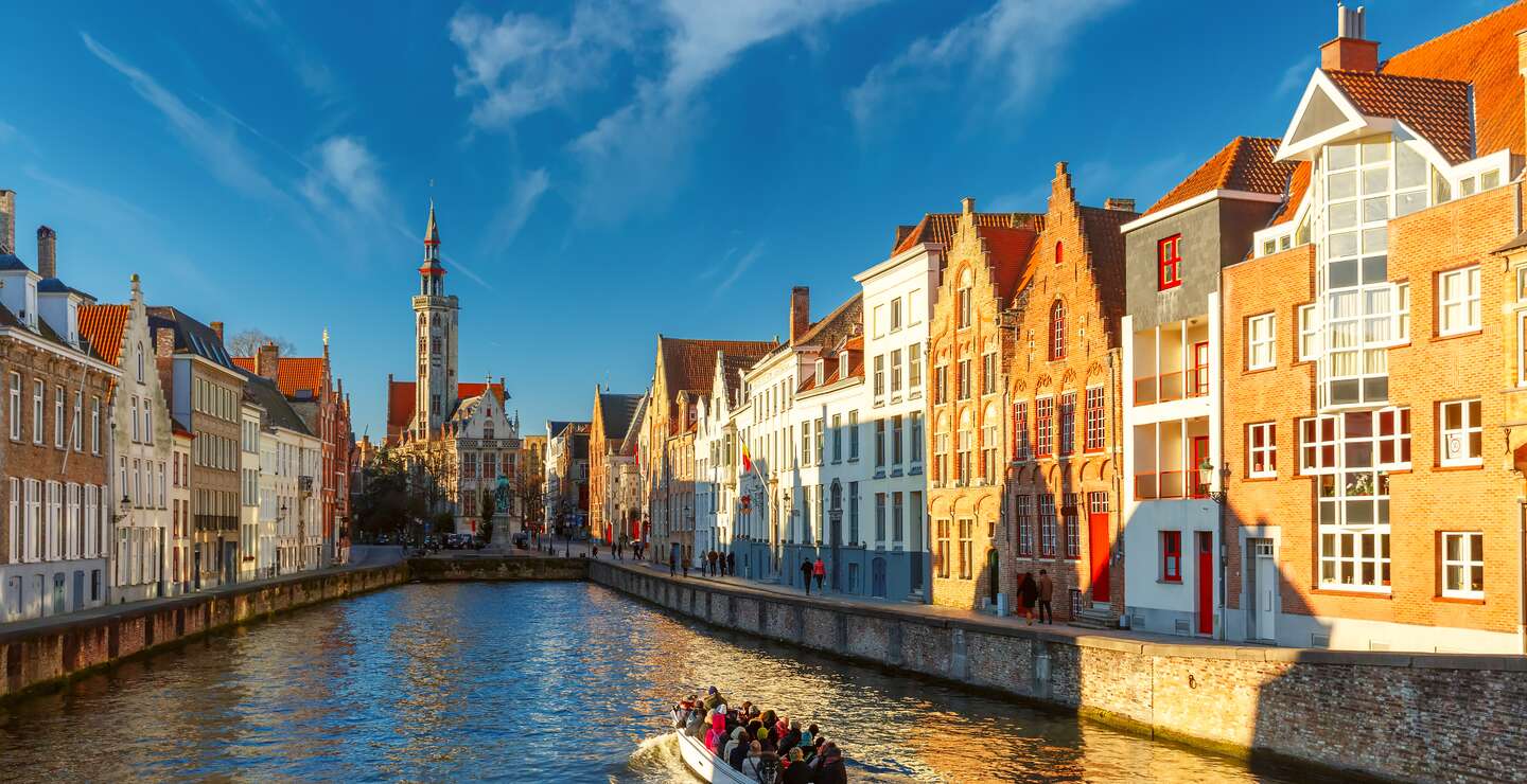 Auf einem Kanal in Bruegge faehrt ein Ausflugsboot. Die historischen Haeuser werden von der Sonne angestrahlt. | © Gettyimages.com/KavalenkavaVolha