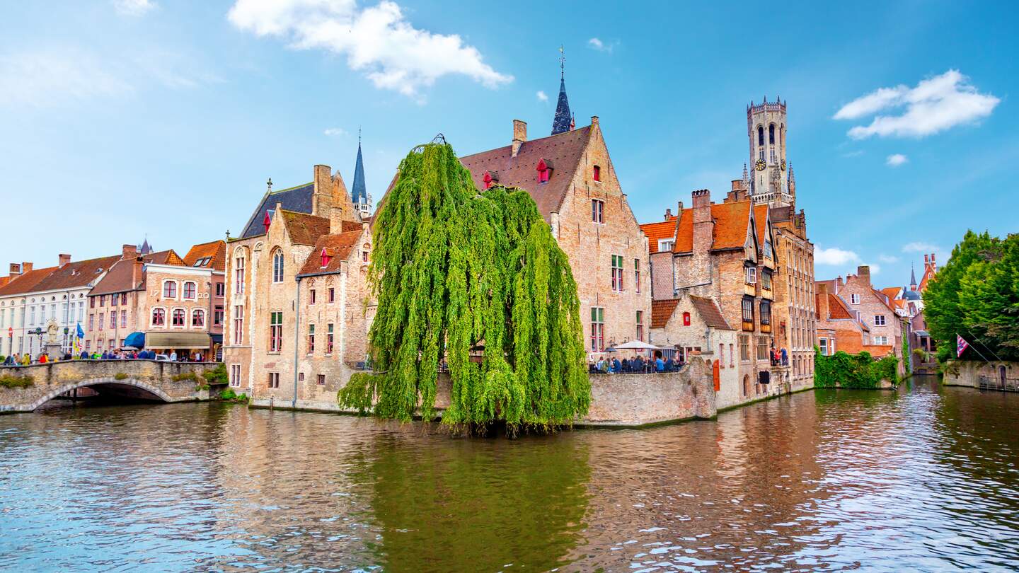 Am Rosenkranz-Quai in Brügge stehen Touristen. Im Hintergrund ist der Belfried. | © Gettyimages.com/adisa