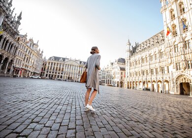 Junge Frau, die auf dem Hauptplatz mit Rathaus in der Altstadt von Bruessel spazieren geht | © Gettyimages.com/RossHelen