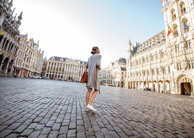 Junge Frau, die auf dem Hauptplatz mit Rathaus in der Altstadt von Bruessel spazieren geht | © Gettyimages.com/RossHelen