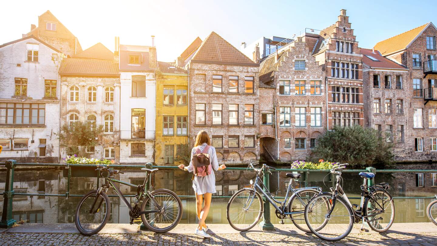 Eine Frau steht in Gent, Belgien an einem Fluss und blickt auf die Altstadt. Neben ihr stehen Fahrräder | © Gettyimages.com/RossHelen