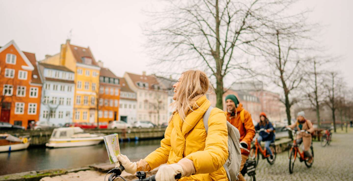 Gruppe Touristen mit dicken Jacken und Muetzen auf Fahrrädern am Hafen in Kopenhagen, Dänemark, vor den beruehmten Nyhavn | © GettyImages.com/AleksandarNakic