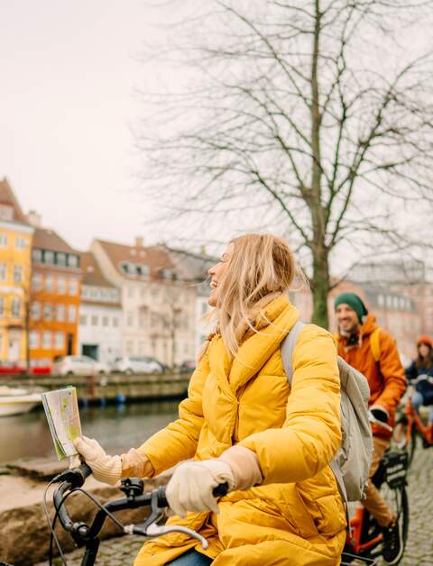 Gruppe Touristen mit dicken Jacken und Muetzen auf Fahrrädern am Hafen in Kopenhagen, Dänemark, vor den beruehmten Nyhavn | © GettyImages.com/AleksandarNakic