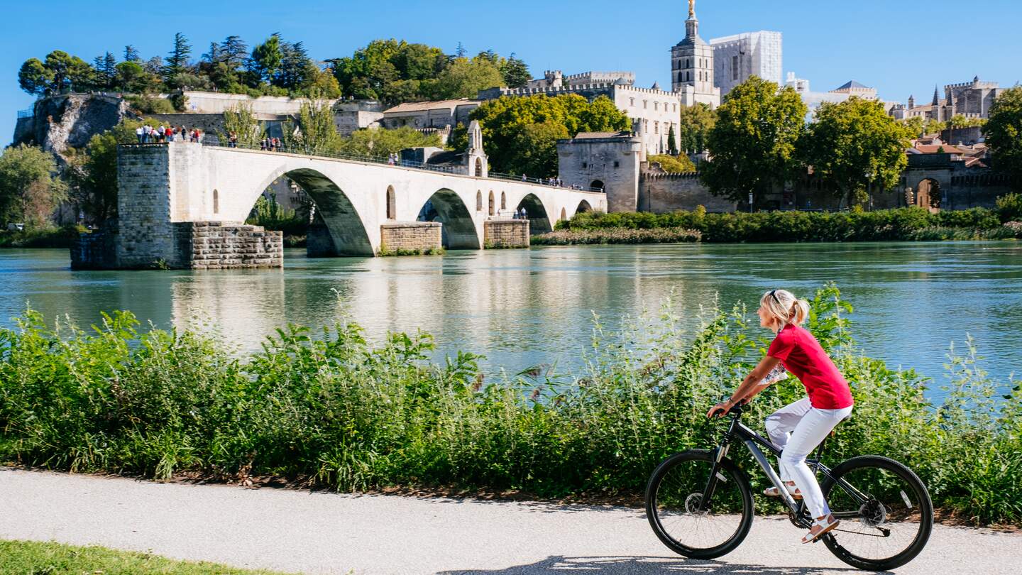 Frau, die von Pont Saint-Bénézet an der Rhone in Avignon in der Provence in Frankreich radelt | © Gettyimages.com/lucentius