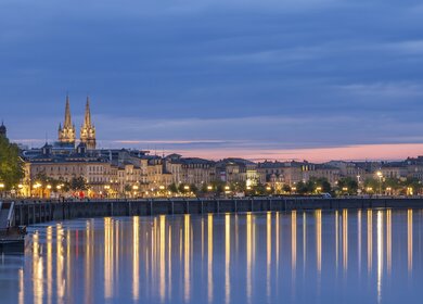 Blick auf Bordeaux am Abend mit Lichtern, die sich im Wasser der Garonne spiegeln | © Gettyimages.com/Leonid Andronov