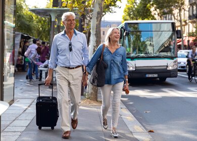 Seniorenpaar, das händehaltend vor dem Bus in Paris läuft. | © Gettyimages.com/LeoPatrizi