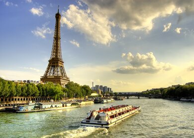 Menschen machen eine Bootsfahrt auf der Seine in Paris, Lastkähne und Bäume bei Sonnenuntergang. | © Gettyimages.com/AleksandarGeorgiev
